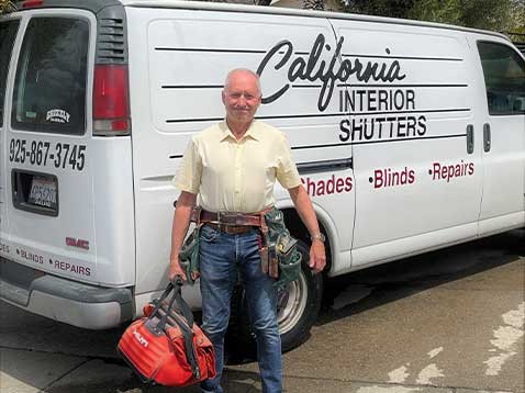 A man wearing a toolbelt carrying a tool bag, standing by the company van